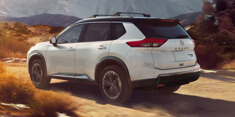 Exterior of a white, 2026 Nissan Rogue driving by a mountain range. 